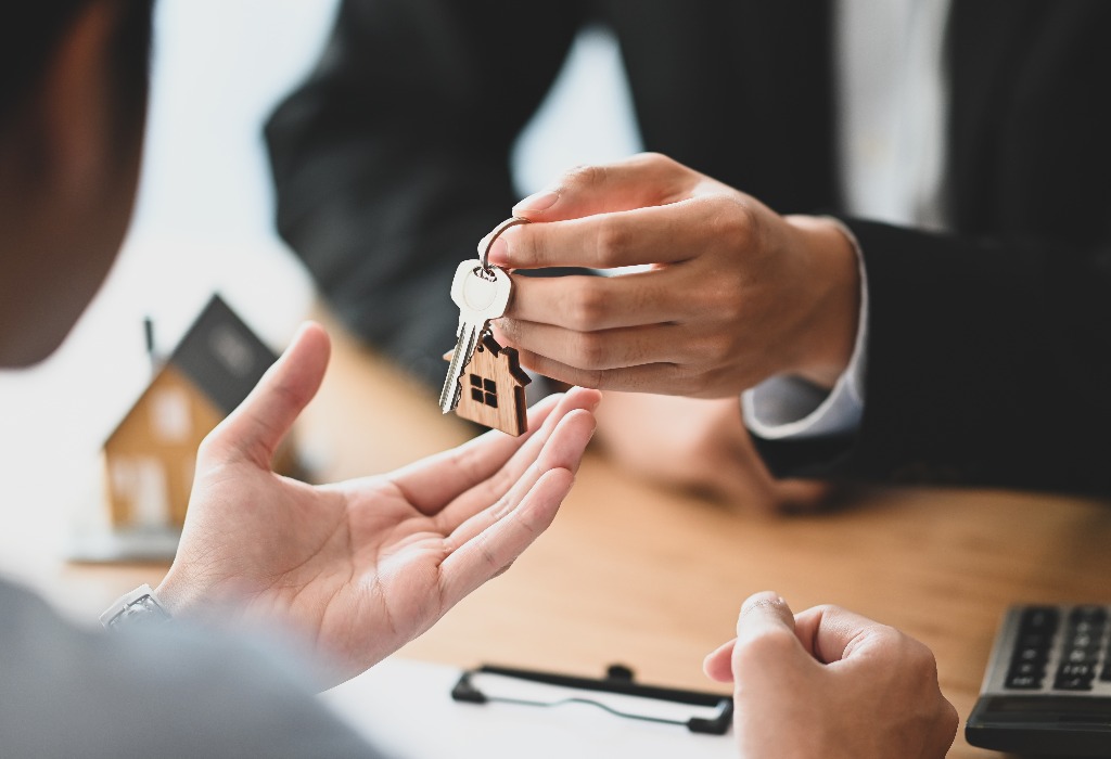 Cropped shot of house broker giving a property key to his customer while he has writing signing on agreement at the modern wooden desk loan debt credit buying or selling agreement concept jpg